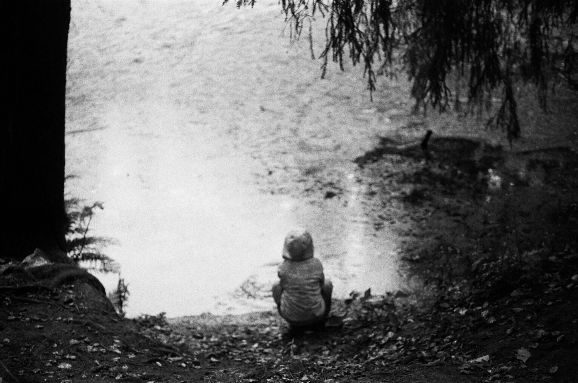 Child crouched beside a lake